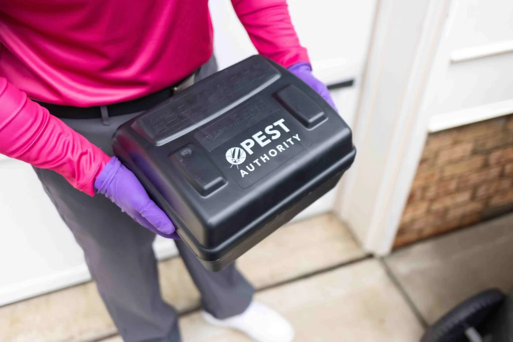 A gloved pest control technician holds a black case with "Pest Authority"